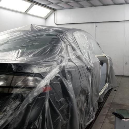 Mit Folie abgedecktes Auto in einer Lackierkabine, vorbereitet für Lackierarbeiten.